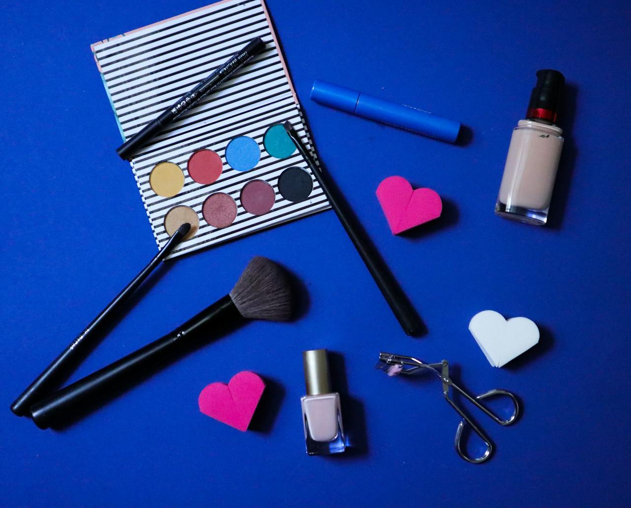 gallery-1 Colorful makeup products arranged stylishly on a blue backdrop for beauty inspiration.