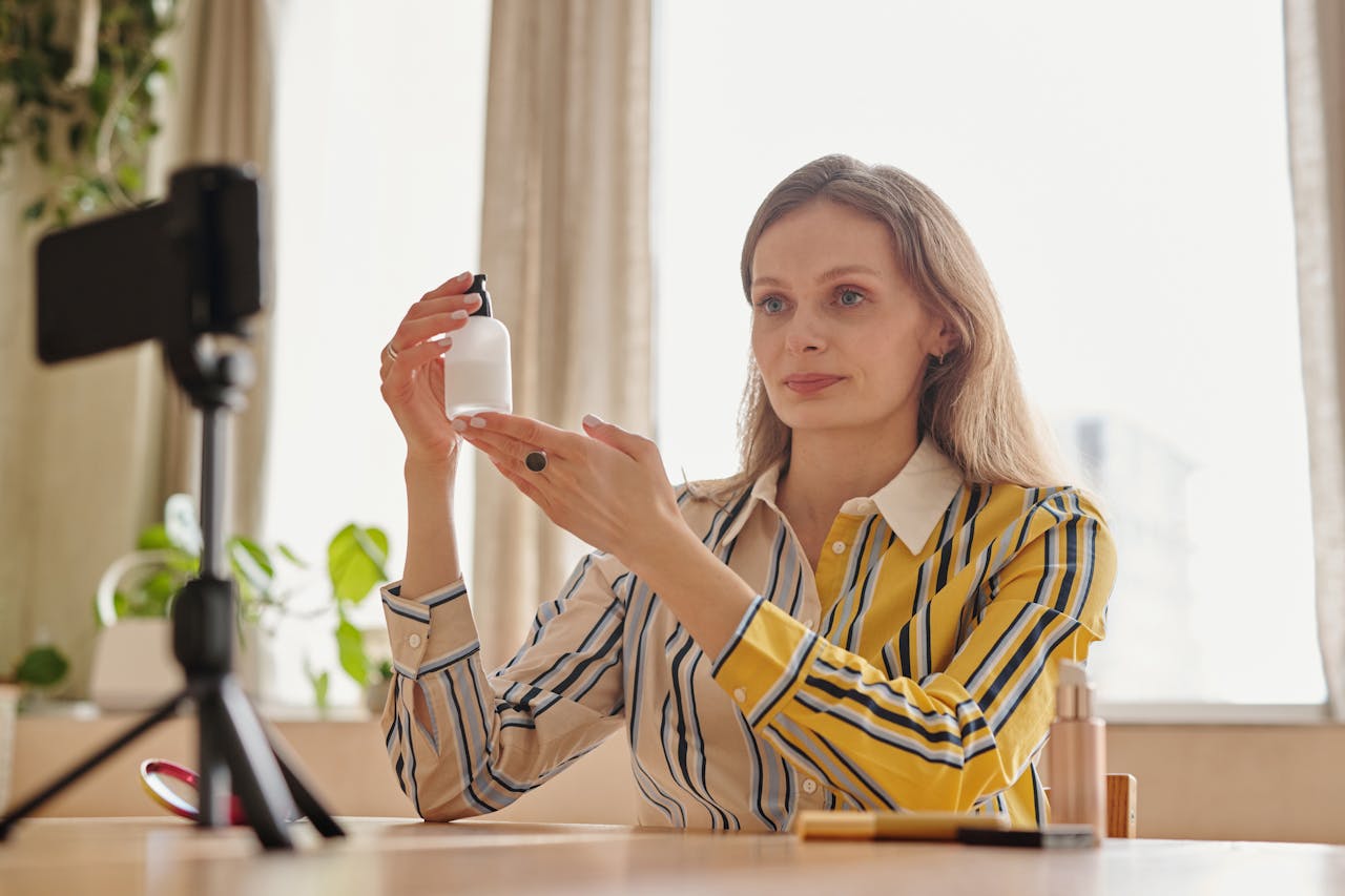 gallery-4 Woman demonstrates skincare product during a vlog in a cozy indoor setting.
